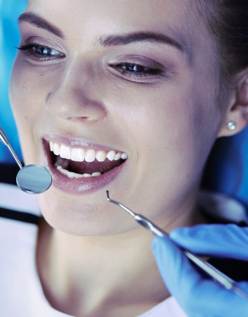Young Female patient with open mouth examining dental inspection at dentist office.