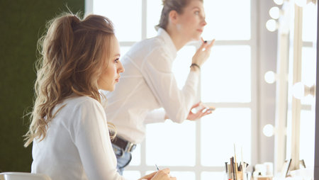 Make-up artist applying white eyeshadow in the corner of models eye and holding a shell with...