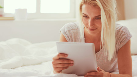Girl holding digital tablet with blank screen and smiling at camera in bedroom