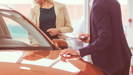 Dealer with woman stands near a new car in the showroomの写真素材