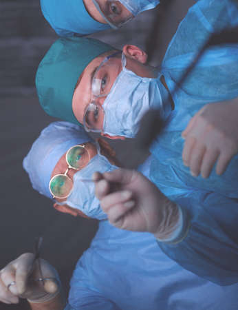 Group of surgeons at work in operating theater toned in blue. Medical team performing operationの写真素材