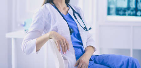 Beautiful female doctor sitting in a consulting room, smiling at the cameraの写真素材