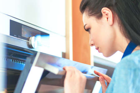 Beautiful young woman checking how her cake is doing in the ovenの写真素材
