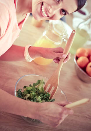 Smiling young woman mixing fresh salad in the kitchen.の写真素材
