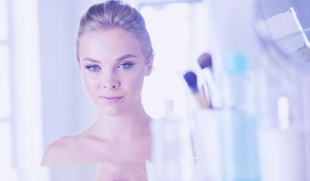 Young woman in bathrobe looking in bathroom mirrorの写真素材