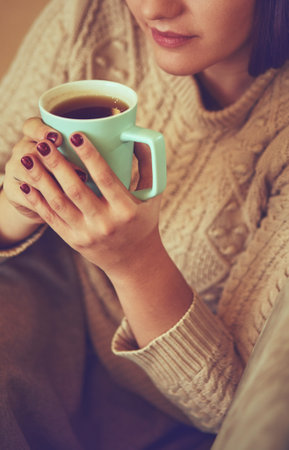 Happy young woman sitting on sofa holding a mug at home in the living roomの写真素材