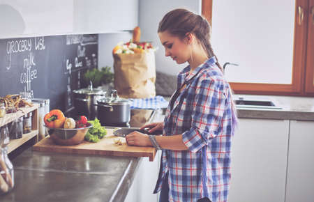 Young woman cutting vegetables in kitchen near deskの写真素材