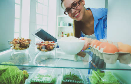 Portrait of female standing near open fridge full of healthy food, vegetables and fruitsの写真素材