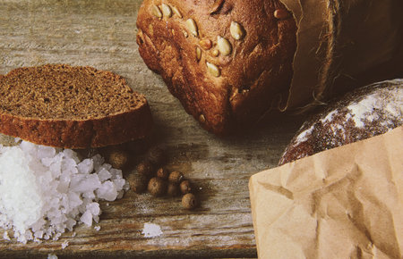 Two Loaves of Bread packed in paper on wooden table with salt and papper. Cropped photo