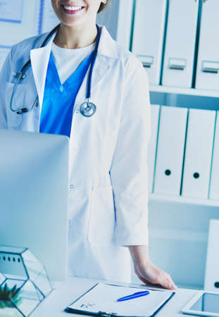 Young doctor woman standing near table, isolated on white backgroundの写真素材