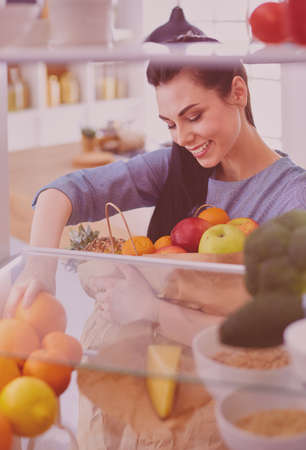 Smiling woman taking a fresh fruit out of the fridge, healthy food conceptの写真素材