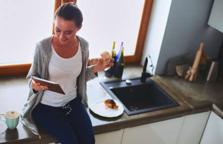 Beautiful young woman using a digital tablet in the kitchenの写真素材