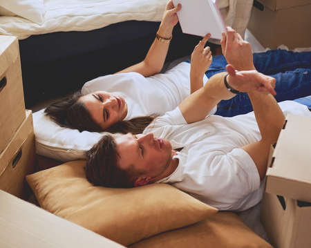 Cute couple unpacking cardboard boxes in their new home, lying on the floor and looking at a family albumの写真素材