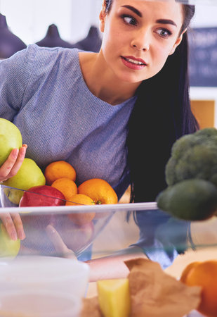 Smiling woman taking a fresh fruit out of the fridge, healthy food concept