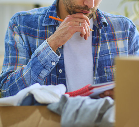 A moving man sitting on the floor in empty apartment, Among the Boxes, Checking the List of Thingsの写真素材