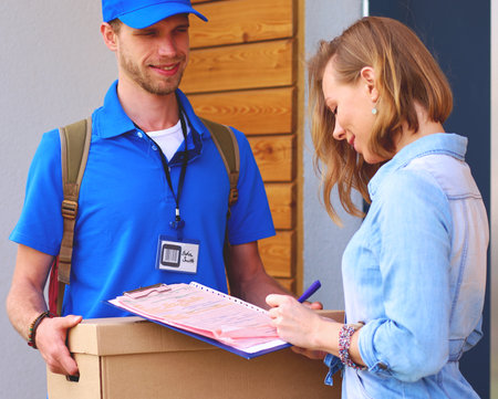 Smiling delivery man in blue uniform delivering parcel box to recipient - courier service concept. Smiling delivery man in blue uniformの写真素材
