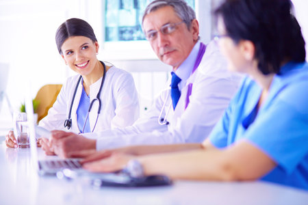 Smiling doctor using a laptop working with her colleagues in a bright hospital roomの写真素材