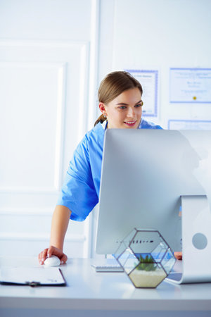Portrait of female physician filling up medical form while standing near reception desk at clinic or emergency hospitalの写真素材