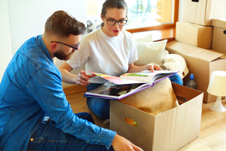 Happy couple looking at photo album while unpacking stuff after relocation to new flatの写真素材