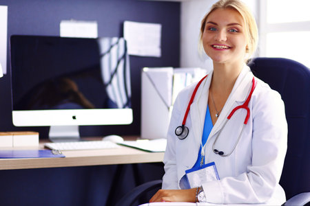 Portrait of young female doctor sitting at desk in hospitalの写真素材