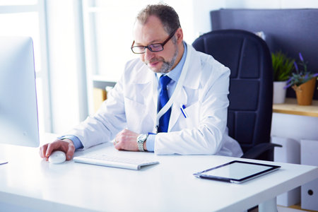 Portrait of senior doctor in office sitting at the deskの写真素材
