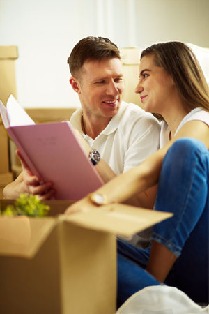 Young couple holding album while sitting on floor in new houseの写真素材