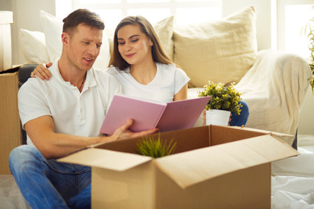 Young couple holding album while sitting on floor in new houseの写真素材