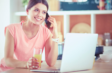 Young woman in kitchen with laptop computer looking recipes, smiling. Food blogger conceptの写真素材