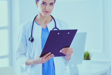 Young smiling female doctor with stethoscope holding a folder at doctors officeの写真素材