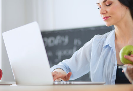 Woman with apple and laptop sitting in the kitchenの写真素材