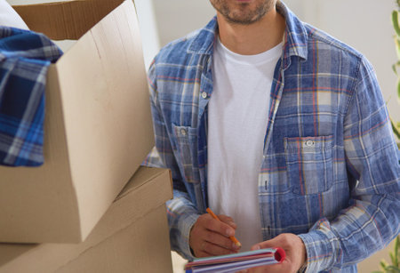 A moving man sitting on the floor in empty apartment, Among the Boxes, Checking the List of Thingsの写真素材