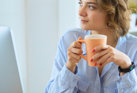 Attractive woman sitting at office desk, holding a cup of coffeeの写真素材