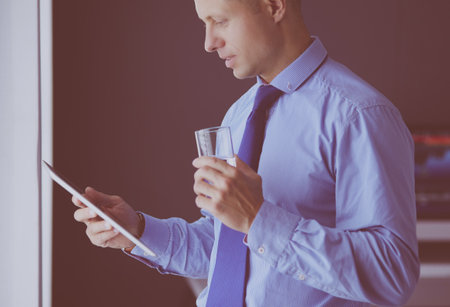 Smiling businessman with touchpad standing at workplace in officeの写真素材