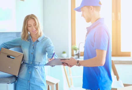 Smiling delivery man in blue uniform delivering parcel box to recipient - courier service concept. Smiling delivery man in blue uniformの写真素材