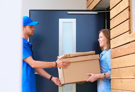 Smiling delivery man in blue uniform delivering parcel box to recipient - courier service concept. Smiling delivery man in blue uniformの写真素材