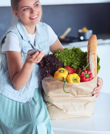 Young woman holding grocery shopping bag with vegetables .Standing in the kitchenの写真素材
