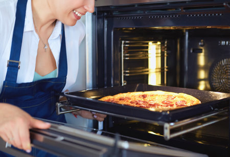 Happy young woman cooking pizza at homeの写真素材