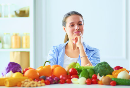 Young and cute woman sitting at the table full of fruits and vegetables in the wooden interior.の写真素材