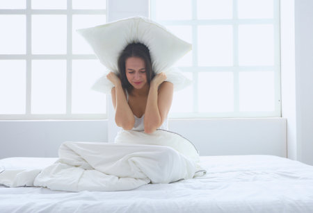 Young caucasian woman covering her head and ears with pillows.の写真素材