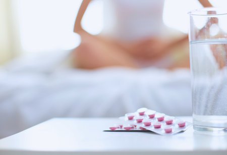 Young beautiful woman with pills lying on bed in bedroomの写真素材