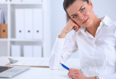 Attractive businesswoman sitting on a desk with laptop in the officeの写真素材