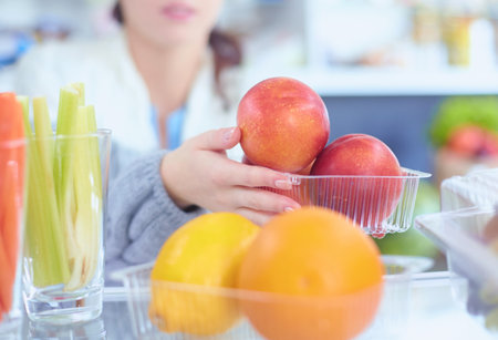 Portrait of female standing near open fridge full of healthy food, vegetables and fruits. Portrait of femaleの写真素材