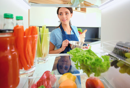 Portrait of female standing near open fridge full of healthy food, vegetables and fruits. Portrait of femaleの写真素材