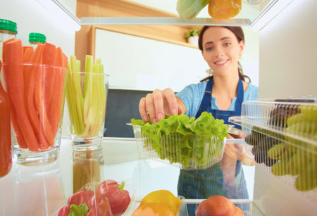 Portrait of female standing near open fridge full of healthy food, vegetables and fruits. Portrait of femaleの写真素材