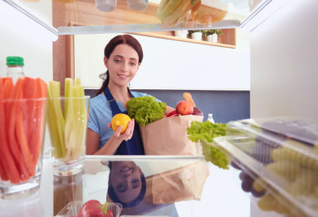 Portrait of female standing near open fridge full of healthy food, vegetables and fruits. Portrait of femaleの写真素材
