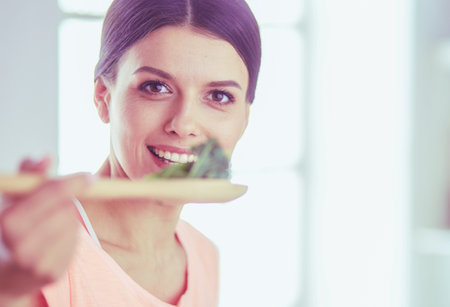 Smiling young woman mixing fresh salad in the kitchen.の写真素材