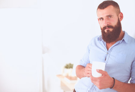 Handsome young Indian man holding coffee cup and smiling while standing against white backgroundの写真素材