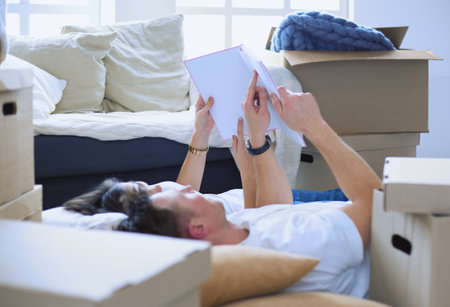 Cute couple unpacking cardboard boxes in their new home, lying on the floor and looking at a family albumの写真素材