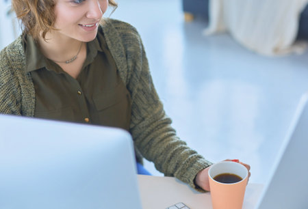 Attractive woman sitting at office desk, holding a cup of coffeeの写真素材