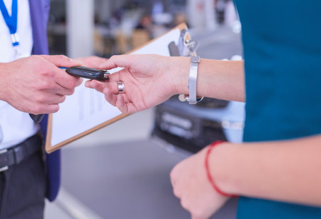 Car salesman sells a car to happy customer in car dealership and hands over the keysの写真素材
